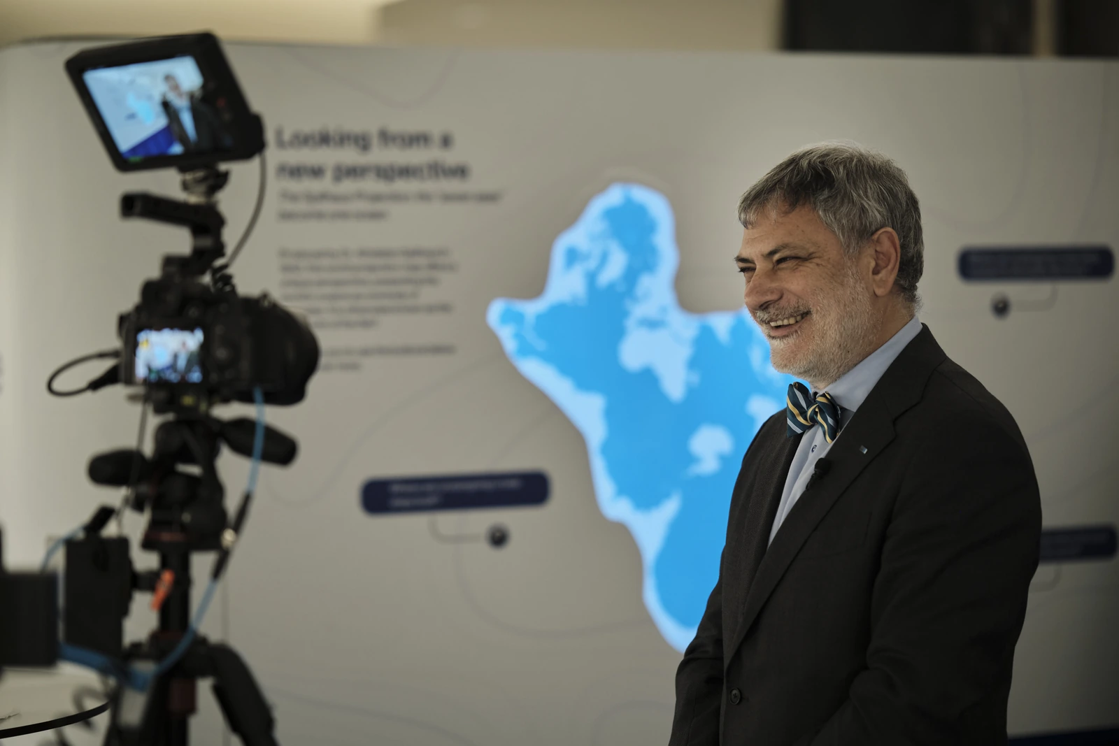 A speaker being filmed for an interview in front of the Spilhaus map